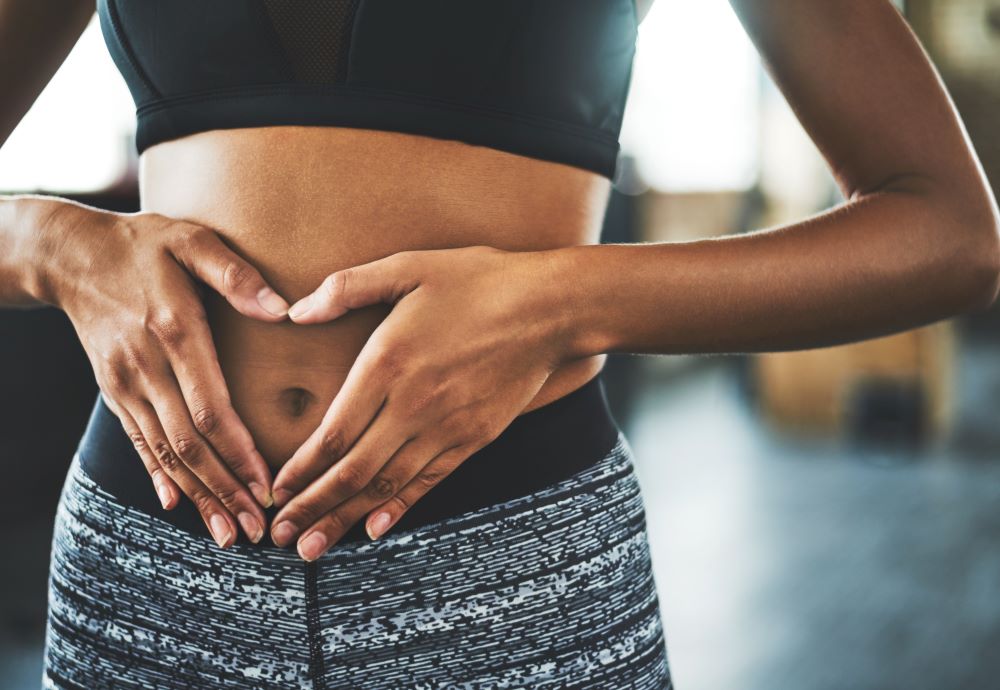 Woman in activewear with hands on stomach in the shape of a heart