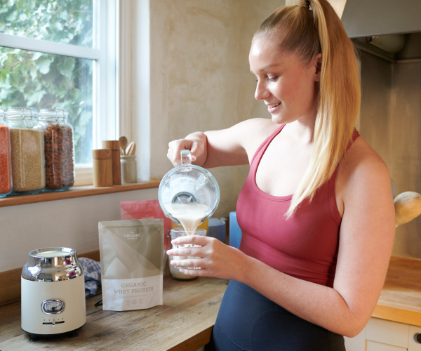 A woman pouring a glass of organic whey protein shake from a blender