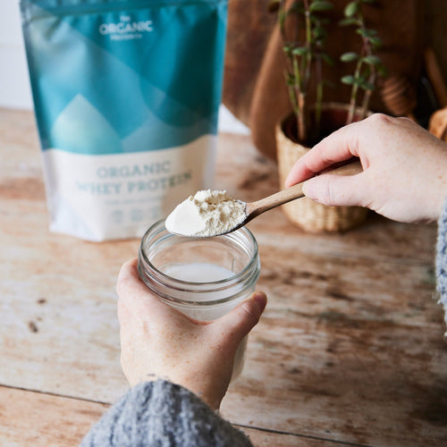 Person putting a spoonful of organic whey protein power into a glass of milk