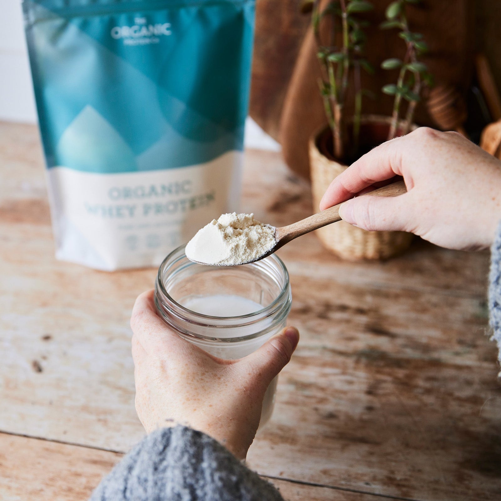 Person putting a spoonful of organic whey protein power into a glass of milk