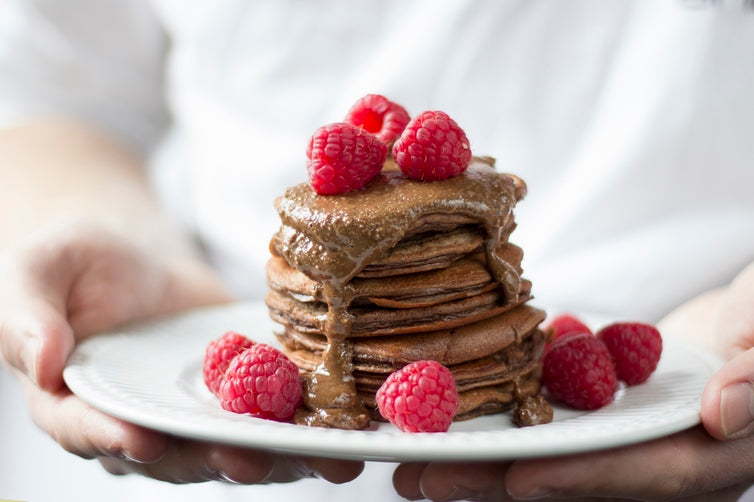 Stack of chocolate protein pancakes on a plate, topped with fresh raspberries and chocolate hazelnut butter